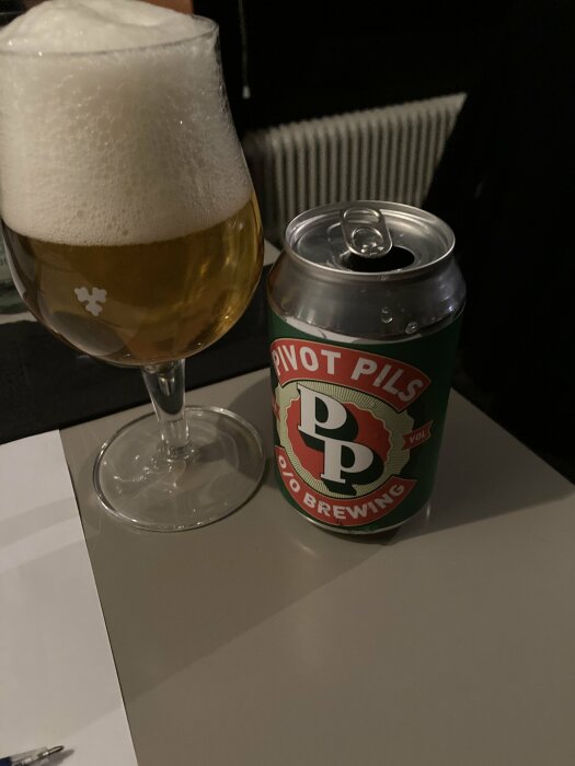 En glas med skummande öl bredvid en öppnad burk märkt "Pivot Pils".