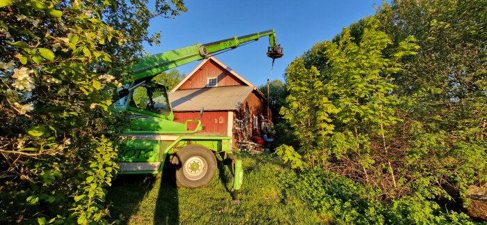 Grön teleskoplastare i arbete vid röd lada omgiven av grönska, används för olika uppgifter på gård efter att ha ersatt önskad skylift.