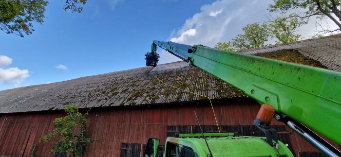 Grön teleskoplastare används för att tvätta ett tak; sett från marken med klarblå himmel i bakgrunden.