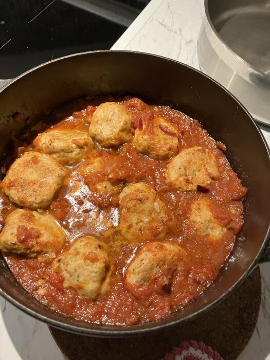 Kycklingbullar i tomatsås i en gryta, förberedda för matlagning.