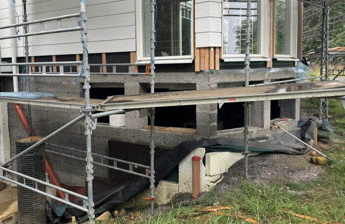 Byggarbetsplats med ställningar vid ett hus med Finja Exakt block i suterräng/källarvåning, förberett för fönsterinstallation.