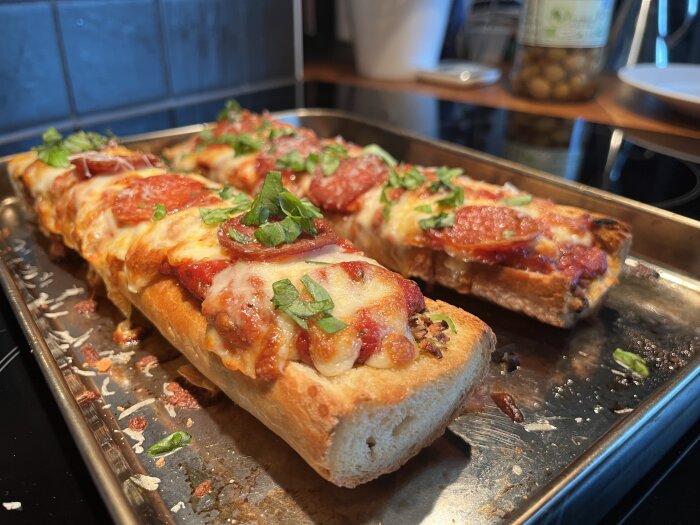 French Bread Pizza med tomatsås, ost, pepparoni och färsk basilika på en plåt.