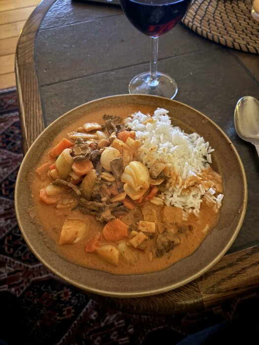 Tallrik med biff och Panangcurry serverad med ris, och ett glas rödvin på ett matbord.