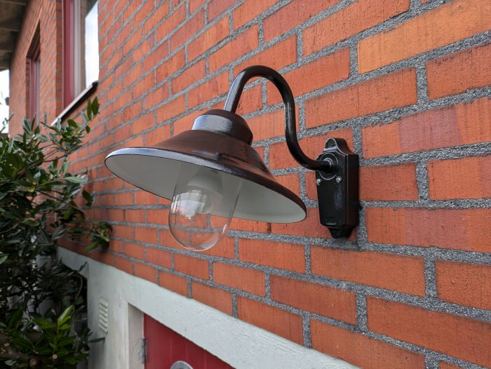 Renoverad utomhuslampa monterad på tegelfasad, nymålad i mörkt metalliskt hammarlack, ny kabel draget och Shellyrelä installerat.