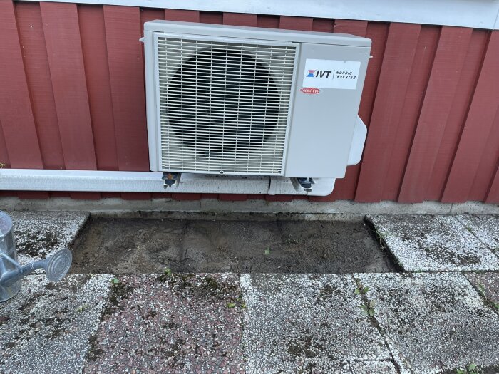 Luftvärmepumpens utedel på fasad med borttagna plattor och blottad jord, förberedelse för dräneringslösning vid radhus i behov av vattenavledning.