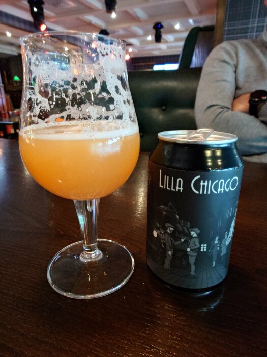 Ett ölglas med ofiltrerad öl och en burk med etikett "Lilla Chicago" på ett bord i en restaurangmiljö.