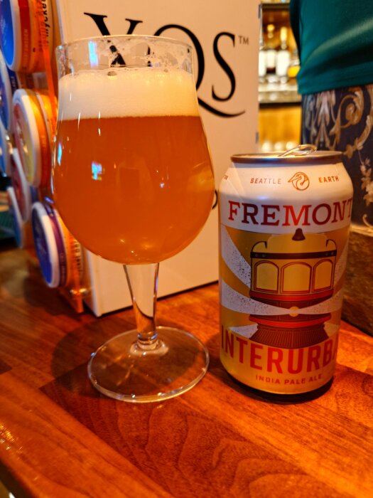 Ett glas öl med skumkrona och en Fremont Interurban IPA-burk på ett träbord.