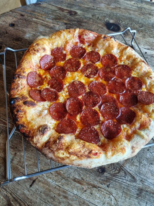 Pizza med pepperoni på färdig deg från Pop bakery, placerad på ett galler ovanpå ett träbord.