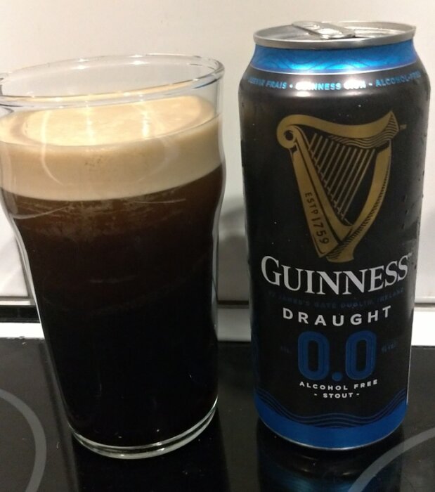 Alkoholfri Guinness 0.0 burk bredvid ett glas med mörk stout och skummig yta.