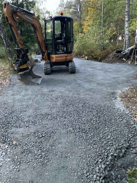 Orange grävmaskin står på en grusväg omgiven av skog, arbete verkar pågå.