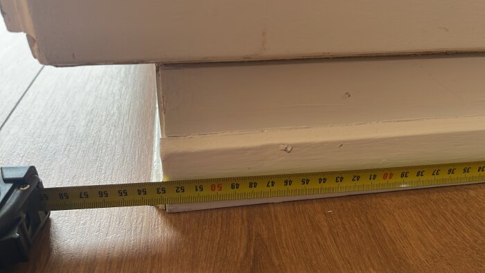 Mäta gammal garderob med måttband på golvet i trä, fokuserar på djupet som visar cirka 51 centimeter.