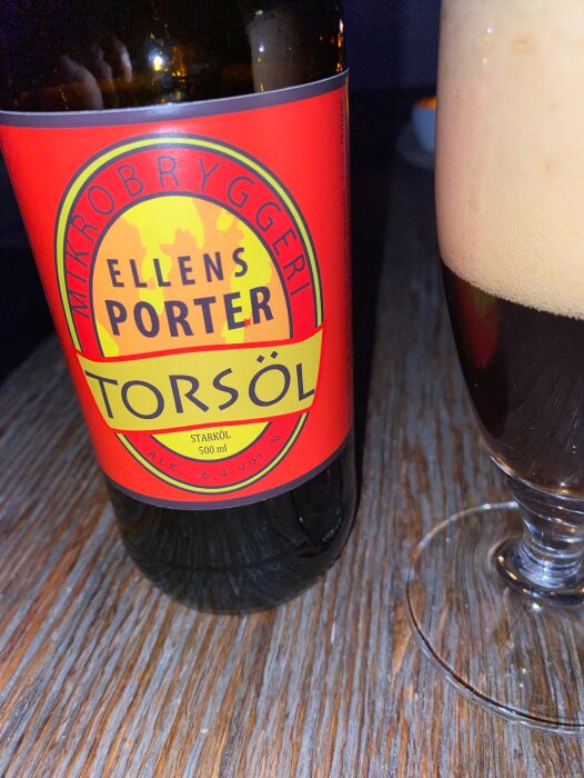 Flaska Ellens Porter från Mikrobryggeri Torsöl och ett glas med skummande porter på ett träbord.