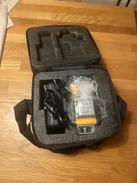 Multilinjelaser DW089LG i en svart väska med tillbehör, inklusive laddare och inplastad huvudenhet, på ett bord.