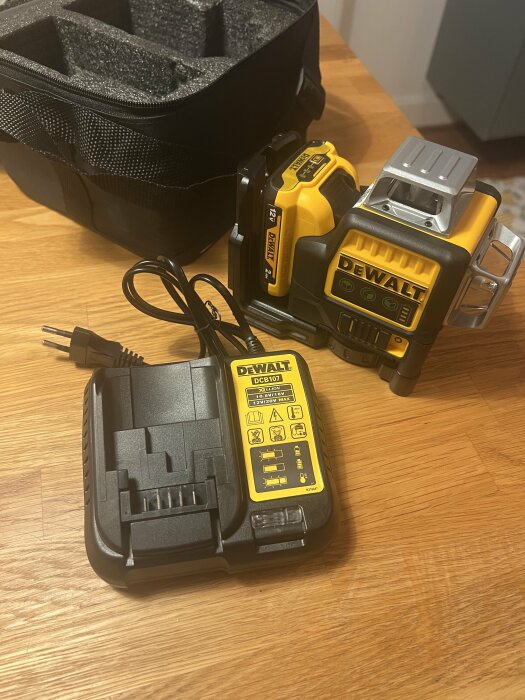 DeWalt multilinjelaser med gul och svart huvudenhet, laddare och svart förvaringsväska på träbord.