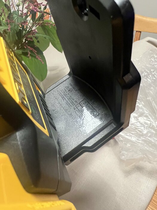 Multilinjelaser med svart bas och gul märkning, står inuti med synlig inskription på botten och en plastförpackning i bakgrunden på ett bord.