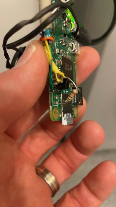 En hand håller i ett Raspberry Pi-kort med anslutna kablar, en resistor och en mikro-SD-kortlösning.