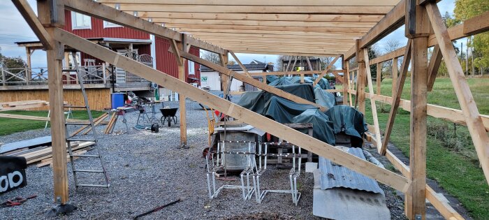 Öppen konstruktion av en vagnslid, med träramar och snedsträvor. Byggmaterial och verktyg syns i förgrunden.