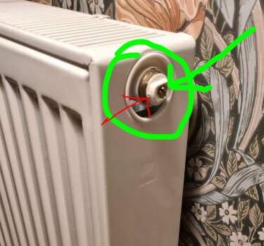 Radiator med luftskruv markerad med gröna pilar; en del av väggen syns i bakgrunden med mönstrad tapet.