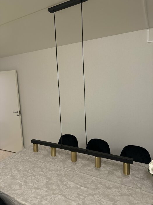 Ny kökslampa med långa snören hänger över matbord med mönstrad duk.