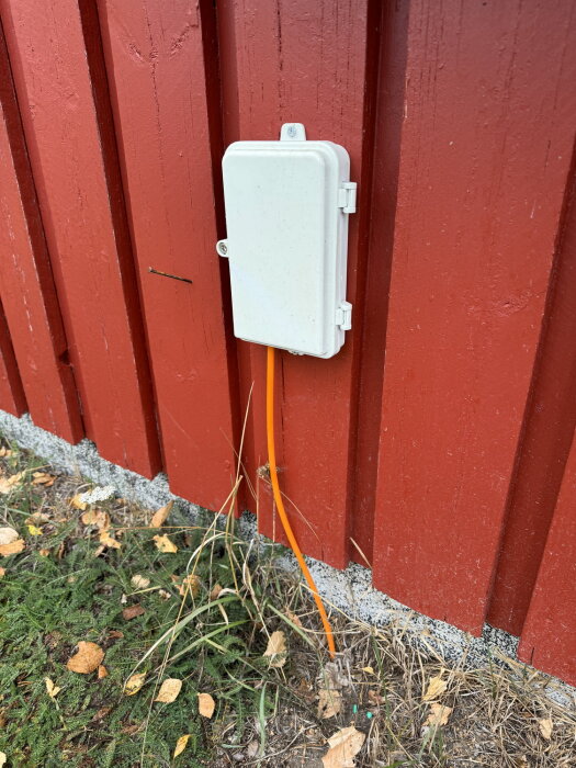 Vit plastlåda med orange fiberkabel monterad på röd husvägg.