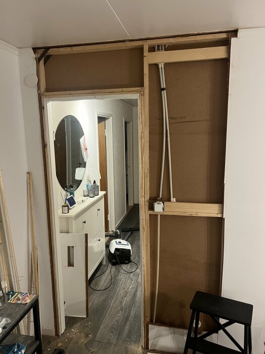 Vägg utan ytterpanel med synliga reglar och rör, lysknapp och spegelbyrå i hallen; fråga om väggen är bärande eller inte.