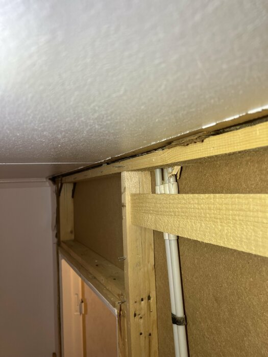 Närbild av en innervägg med träreglar vid en dörröppning, visar trästruktur och några synliga kablar.