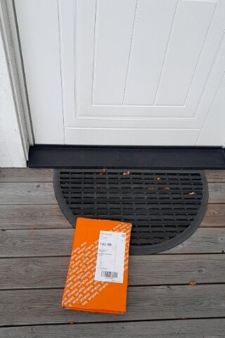 Vått oranget Bokus-paket ligger vid ytterdörren på en grå träveranda med en matta, levererat av Citymail.