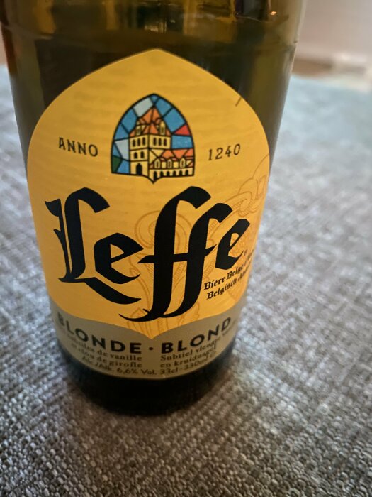 En flaska Leffe Blonde öl med etikett som visar ett ålderdomligt hus och texten "Anno 1240".