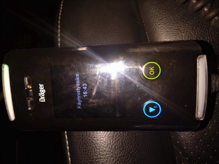 En Dräger alkoholmätare visar tidpunkten 16:43 med knappar markerade OK och start på en brun läderyta.