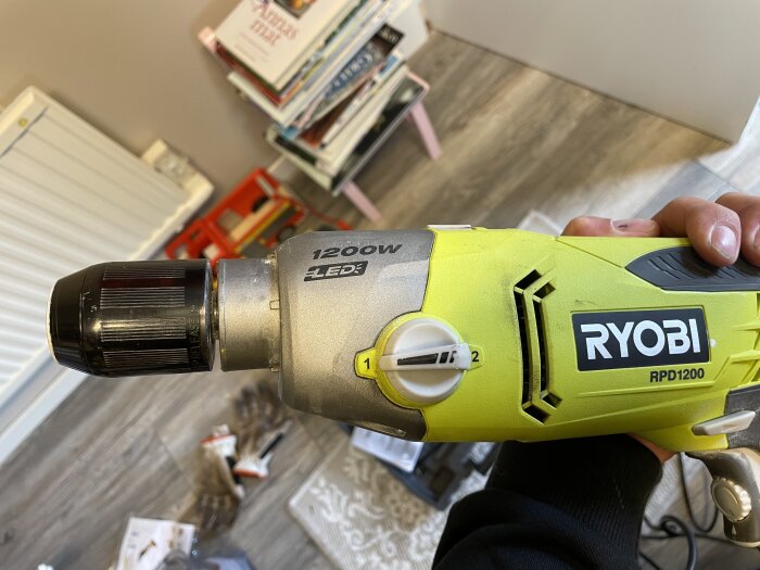 En Ryobi RPD 1200 borrmaskin med en fastkilad chuck hålls i handen, omgiven av verktyg och handskar.