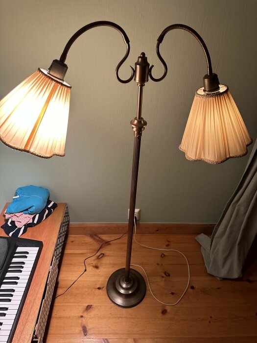 Golvlampa med två tända skärmar, står bredvid ett piano och är inkopplad i väggen.