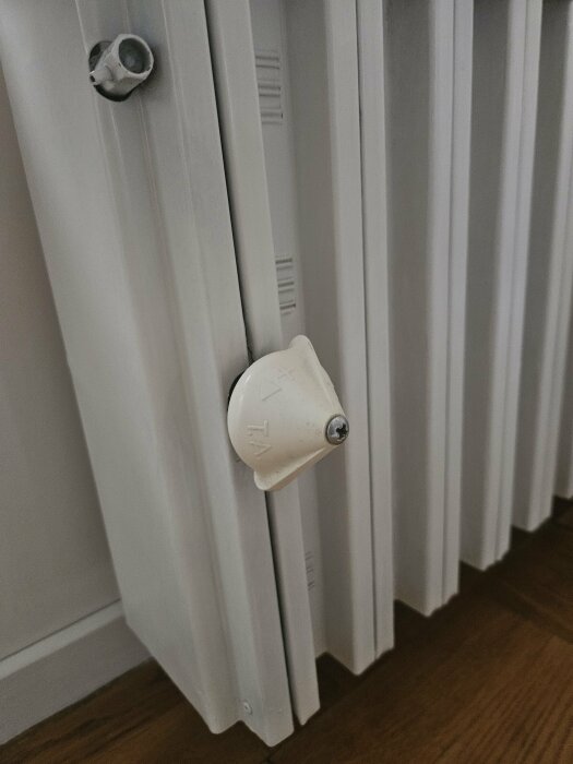 Radiatorfotografering med närbild på en vit termostatventil och en anslutning som visar där läckage verkar uppstå.