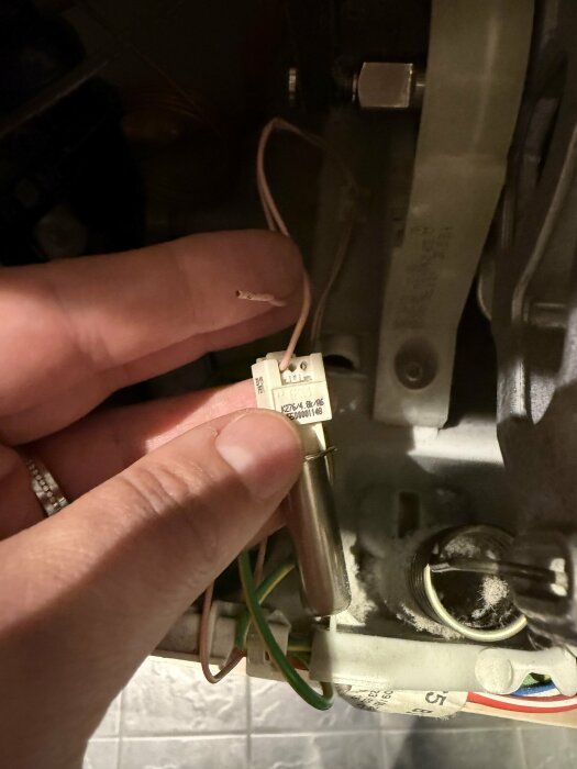 Närbild på en hand som håller i en kabel, visar kabelbrott som har orsakats felkod E09, med en elektrisk komponent i bakgrunden.