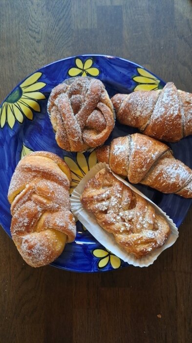 En tallrik med olika bakverk: kanelbullar, croissanter och wienerbröd, strödd med florsocker.