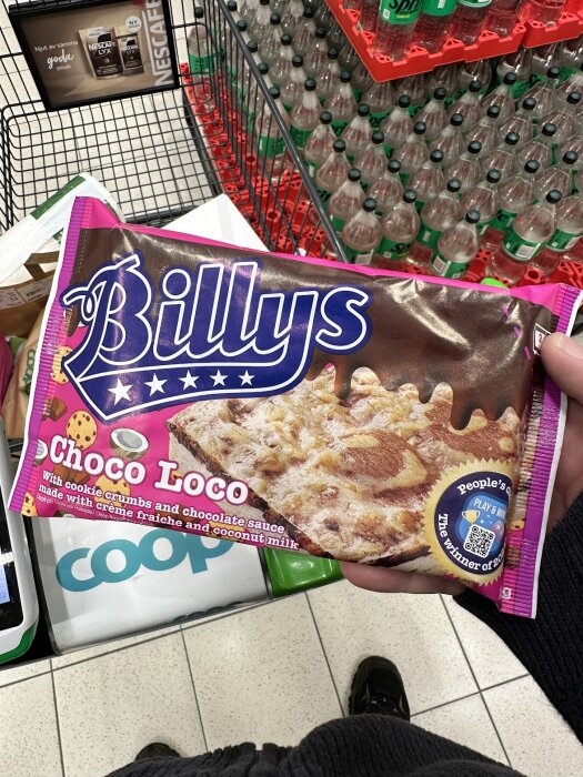 Förpackning av Billys Choco Loco pizza i en kundvagn på en Coop-butik, omgiven av flaskor med dryck.