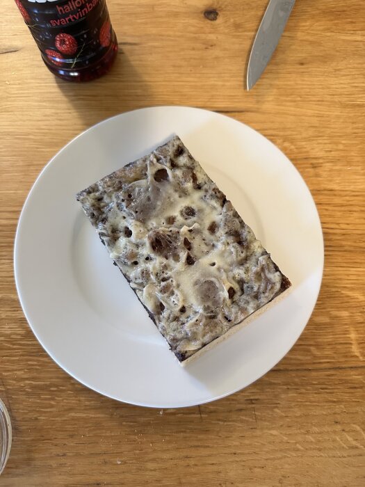 Bröd eller kaka med mögelliknande yta på tallrik, flaska hallon- och svartvinbärsjuice samt kniv på träbord.