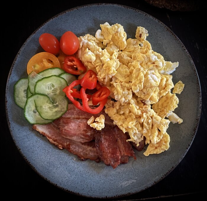 Tallerken med äggröra, stekfläsk, skivad gurka, körsbärstomater och paprika.