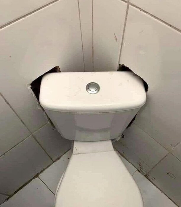 Toalett cistern monterad i hörn med hål i omliggande kakel för att passa in.