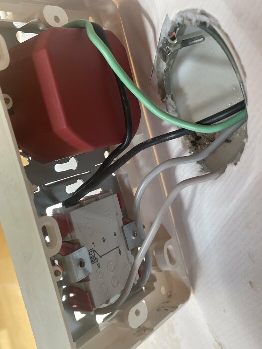 Närbild av elinstallation med vridströmbrytare och kablar i en väggmonterad dosa bakom en förhöjningsram.