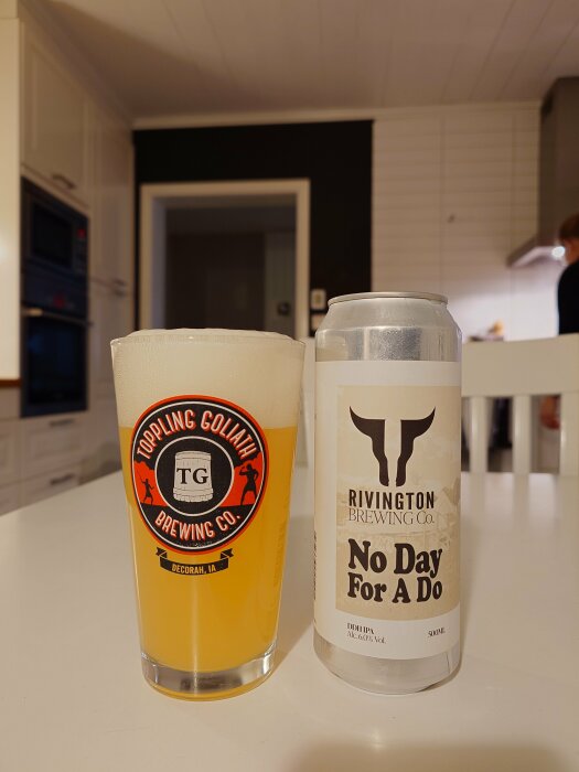 Ölglas med logotypen Toppling Goliath bredvid en burk med texten Rivington Brewing Co. No Day For A Do, i ett kök.