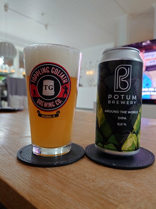 Ett glas öl från Toppling Goliath Brewing Co. och en burk Potum Brewery DIPA på ett bord, med en TV i bakgrunden.