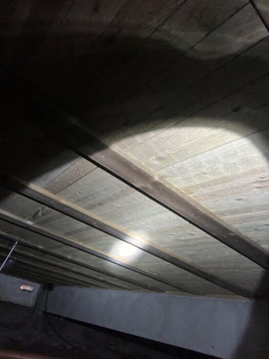 Bild av ett träbjälklag i svag belysning, där en pöl har uppstått på grund av oklart vattenläckage i ett hus från 1983.