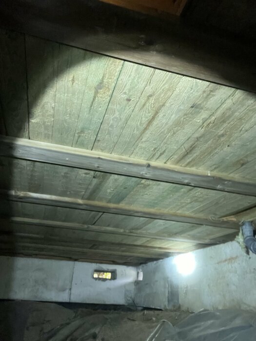 Bild av en källargrund med träplankor och betongvägg, delvis upplyst. Potentiell fuktproblem diskuterat i forumtråd om byggprojekt.