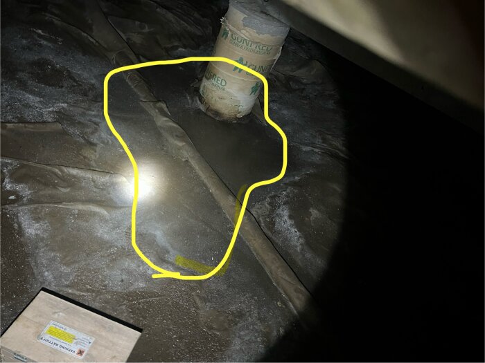 Golv i källare med en gul markering och en ljuskälla, misstänkt vattenläckage syns.