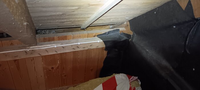 Ett snedtak med träplankor, synlig kutterspån och svart byggplast; isoleringsfrågor om ventilering diskuteras.