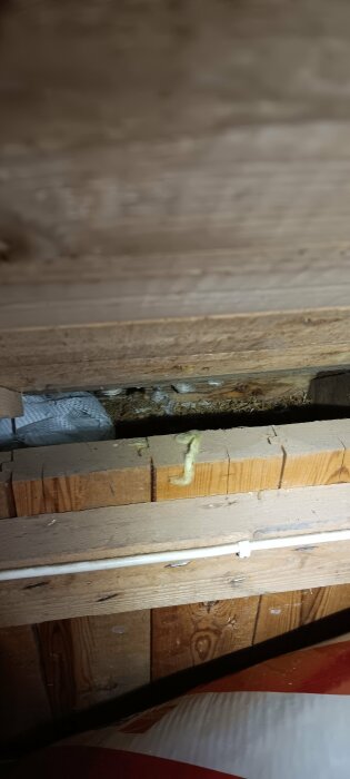 Kattvind med synlig sågspån, träreglar och rör i närheten av takfoten.