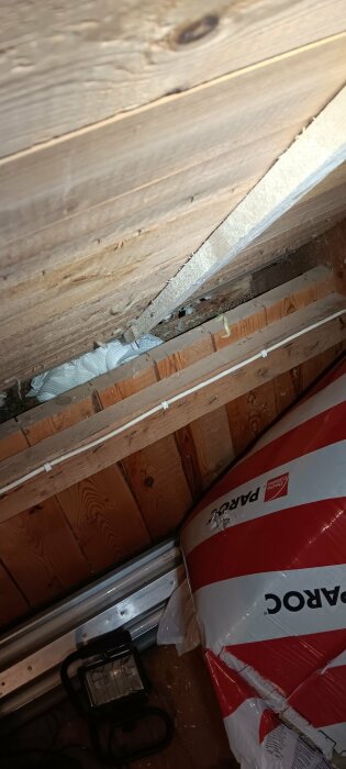 Träpanel och isolering i kattvind med redskap och isoleringsmaterial placerade i ett trångt utrymme.