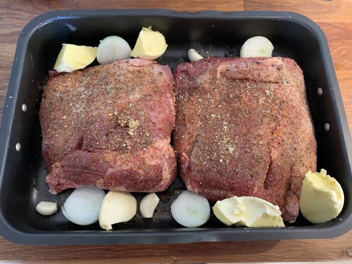 Ugnsform med kryddad köttbit, smör, lök och vitlök, redo för tillagning.