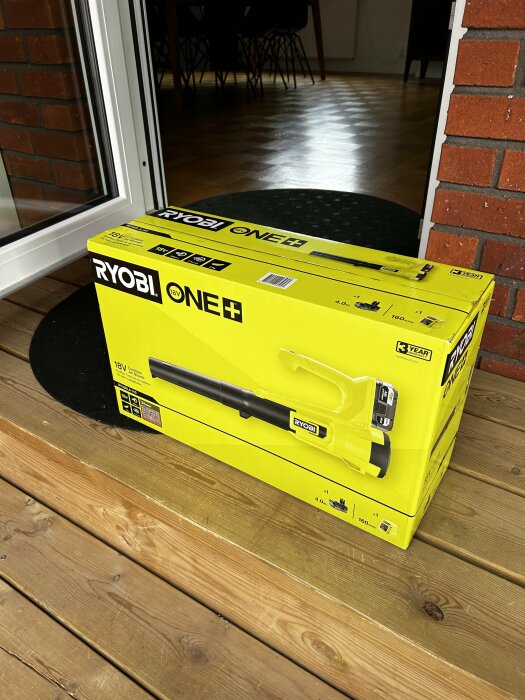 Kartong med en Ryobi One+ lövblåsare på en altan, används för att blåsa bort björkfrön och rengöra garage.