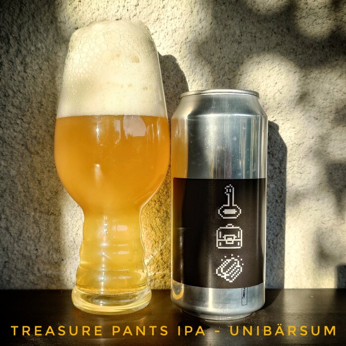 Glas med skummande guldrig dryck bredvid en burk med etikett märkt "Treasure Pants IPA - Unibärsum".